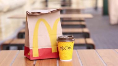Kyiv, Ukrayna - 19 Mart 2024: Üzerinde McDonalds 'ın fast food restoranı logosu ve sokaktaki masada bir fincan kahve olan bir kağıt torba. Bulanık arka planda paket yemek torbası. Latte