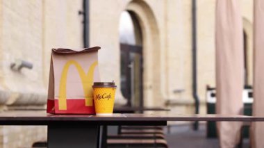Kyiv, Ukrayna - 19 Mart 2024: Üzerinde McDonalds 'ın fast food restoranı logosu ve sokaktaki masada bir fincan kahve olan bir kağıt torba. Bulanık arka planda paket yemek torbası. Latte