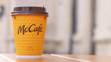 Kyiv, Ukrayna - 19 Mart 2024: Sokaktaki masada üzerinde McDonald 's fast food restoran logosu olan bir kağıt bardak latte. Arka planda bulanık bir kahve. Sarı, tek kullanımlık bardakta Latte.