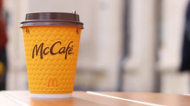 Kyiv, Ukrayna - 19 Mart 2024: Sokaktaki masada üzerinde McDonald 's fast food restoran logosu olan bir kağıt bardak latte. Arka planda bulanık bir kahve. Sarı, tek kullanımlık bardakta Latte.