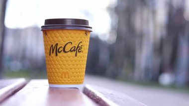 Kyiv, Ukrayna - 19 Mart 2024: Caddedeki bankta üzerinde McDonald 's fast food restoran logosu olan bir kağıt latte fincanı. Arka planda bulanık bir kahve. Tek kullanımlık sarı karton bardakta Latte.