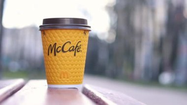 Kyiv, Ukrayna - 19 Mart 2024: Caddedeki bankta üzerinde McDonald 's fast food restoran logosu olan bir kağıt latte fincanı. Arka planda bulanık bir kahve. Tek kullanımlık sarı karton bardakta Latte.