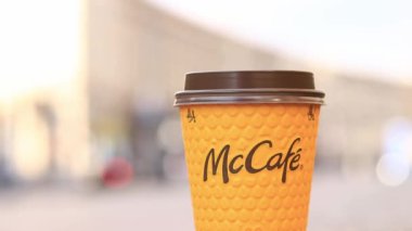 Kyiv, Ukrayna - 19 Mart 2024: Caddelerde McDonald 's fast food restoran logosu olan kağıt latte bardağı. Arka planda bulanık bir kahve. Tek kullanımlık sarı karton bardakta Latte. Kahve içmeye.