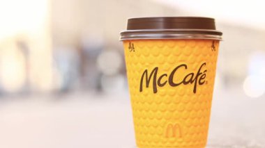 Kyiv, Ukrayna - 19 Mart 2024: Caddelerde McDonald 's fast food restoran logosu olan kağıt latte bardağı. Arka planda bulanık bir kahve. Tek kullanımlık sarı karton bardakta Latte. Kahve içmeye.