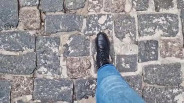 Kot pantolonlu kadın bacakları kaldırım taşı yolda yürüyor, birinci şahıs manzaralı. Sokakta yürürken insan ayağına yakın çekim. Tarihi taş kaldırım taşı sokağının en üst manzarası