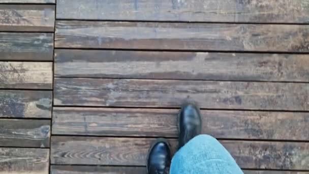 一个女人的脚沿着木板铺成的小径行走 第一眼看到 走在街上的人类脚的特写 在春秋阳光灿烂的日子里散步 从上方看 木地板 木地板 — 图库视频影像
