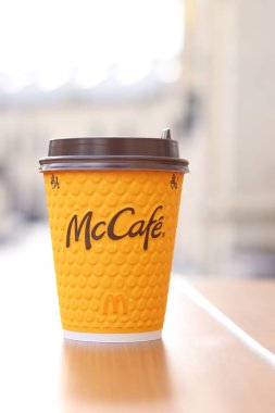 Kyiv, Ukrayna - 19 Mart 2024: Sokaktaki masada üzerinde McDonald 's fast food restoran logosu olan bir kağıt bardak latte. Arka planda bulanık bir kahve. Sarı, tek kullanımlık bardakta Latte.