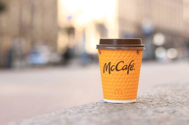 Kyiv, Ukrayna - 19 Mart 2024: Caddelerde McDonald 's fast food restoran logosu olan kağıt latte bardağı. Arka planda bulanık bir kahve. Tek kullanımlık sarı karton bardakta Latte. Kahve içmeye.