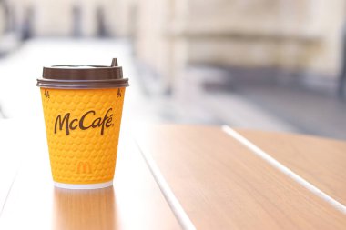Kyiv, Ukrayna - 19 Mart 2024: Sokaktaki masada üzerinde McDonald 's fast food restoran logosu olan bir kağıt bardak latte. Arka planda bulanık bir kahve. Sarı, tek kullanımlık bardakta Latte.