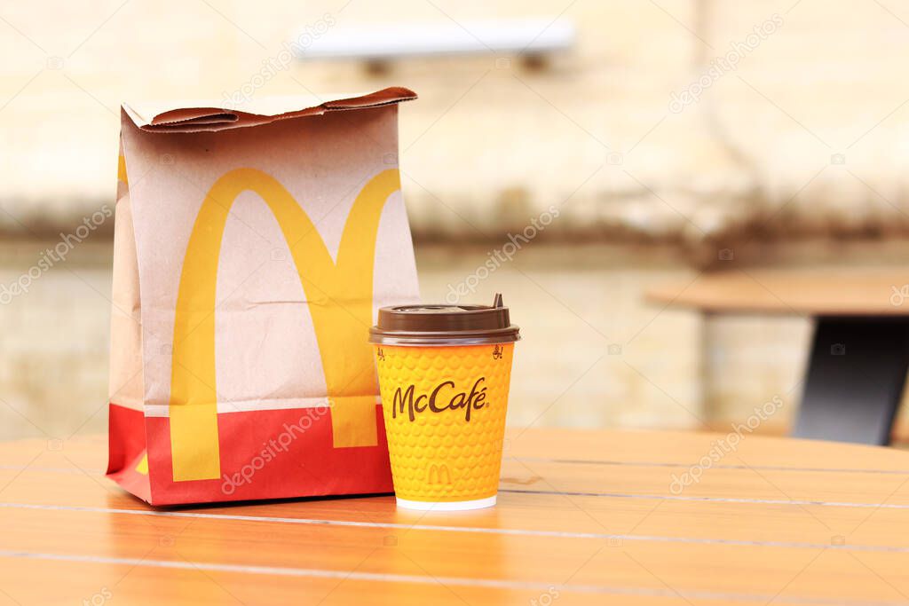 Kyiv, Ukraine - March 19, 2024: A paper bag with the McDonald's fast food restaurant logo and a cup of coffee on a table on the street. Paper bag with takeaway food on blurred background. Latte
