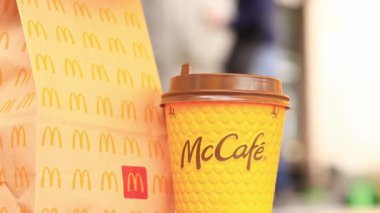 Kyiv, Ukrayna - 22 Mart 2024: İçinde McDonald 's fast food restoranından alınmış yiyecekler ve tek kullanımlık sarı karton bardakta bir latte olan bir kağıt torba. Verandada fast food. Kahveli karton bardak.