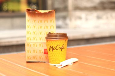 Kyiv, Ukrayna - 22 Mart 2024: İçinde McDonald 's fast food restoranından alınmış yiyecekler ve tek kullanımlık sarı karton bardakta bir latte olan bir kağıt torba. Verandada fast food. Kahveli karton bardak.
