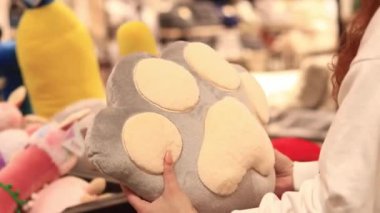 Kyiv, Ukrayna - 26 Mart 2024: Kadın elleri kedi pençesi şeklinde pelüş bir yastık tutuyor, yakın plan. Mağazada oyuncak satmak. Pofuduk bir oyuncak seçen bir alıcının yakın çekimi