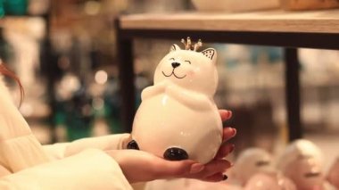 Kyiv, Ukrayna - 26 Mart 2024 Kedi şekilli bozuk para bankası. Kadın eli kedi kumbarası tutuyor, yakın plan. Mağazada ev için satış. Dekor seçen alıcının yakın plan görüntüsü