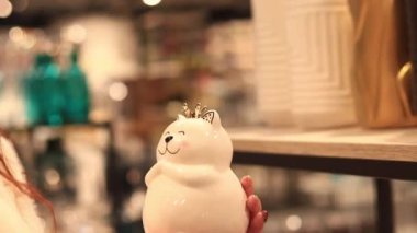 Kyiv, Ukrayna - 26 Mart 2024 Kedi şekilli bozuk para bankası. Kadın eli kedi kumbarası tutuyor, yakın plan. Mağazada ev için satış. Dekor seçen alıcının yakın plan görüntüsü