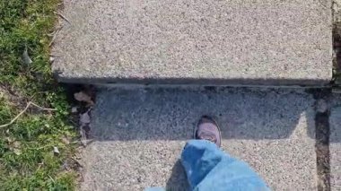 Basamakları tırmanan insan ayaklarına yakın çekim. Bahar ya da yaz aylarında parkta yürüyüş. Yürüyüş. Kot pantolonlu ve spor ayakkabılı bir kadın parkta yürüyor, levhalardan basamaklar.