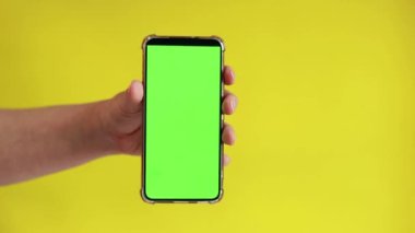 Elinde akıllı telefondan krom anahtar modeli var. Uygulama veya web sitesi tasarımı için kopya alanı gösteriliyor. Sarı arka planda boş yeşil ekranlı akıllı telefon tutan bir kadın var.