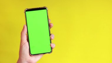 Elinde akıllı telefondan krom anahtar modeli var. Uygulama veya web sitesi tasarımı için kopya alanı gösteriliyor. Sarı arka planda boş yeşil ekranlı akıllı telefon tutan bir kadın var.