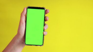 Elinde akıllı telefondan krom anahtar modeli var. Uygulama veya web sitesi tasarımı için kopya alanı gösteriliyor. Sarı arka planda boş yeşil ekranlı akıllı telefon tutan bir kadın var.