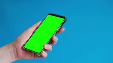 Elinde akıllı telefondan krom anahtar modeli var. Uygulama veya web sitesi tasarımı için kopya alanı gösteriliyor. Bir kadın elinde mavi arka planda boş yeşil ekranlı akıllı bir telefon tutuyor.