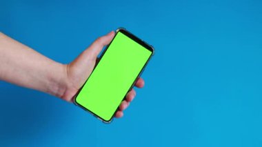 Elinde akıllı telefondan krom anahtar modeli var. Uygulama veya web sitesi tasarımı için kopya alanı gösteriliyor. Bir kadın elinde mavi arka planda boş yeşil ekranlı akıllı bir telefon tutuyor.