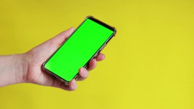 Elinde akıllı telefondan krom anahtar modeli var. Uygulama veya web sitesi tasarımı için kopya alanı gösteriliyor. Sarı arka planda boş yeşil ekranlı akıllı telefon tutan bir kadın var.