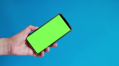 Elinde akıllı telefondan krom anahtar modeli var. Uygulama veya web sitesi tasarımı için kopya alanı gösteriliyor. Bir kadın elinde mavi arka planda boş yeşil ekranlı akıllı bir telefon tutuyor.