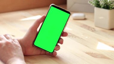 Elinde akıllı telefondan krom anahtar modeli var. Uygulama veya web sitesi tasarımı için kopya alanı gösteriliyor. Ahşap masa arkasında boş yeşil ekranlı akıllı telefonu olan bir kadın. Akıllı telefonun yakın plan görüntüsü