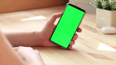 Elinde akıllı telefondan krom anahtar modeli var. Uygulama veya web sitesi tasarımı için kopya alanı gösteriliyor. Ahşap masa arkasında boş yeşil ekranlı akıllı telefonu olan bir kadın. Akıllı telefonun yakın plan görüntüsü