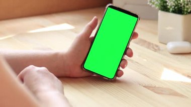 Elinde akıllı telefondan krom anahtar modeli var. Uygulama veya web sitesi tasarımı için kopya alanı gösteriliyor. Ahşap masa arkasında boş yeşil ekranlı akıllı telefonu olan bir kadın. Akıllı telefonun yakın plan görüntüsü