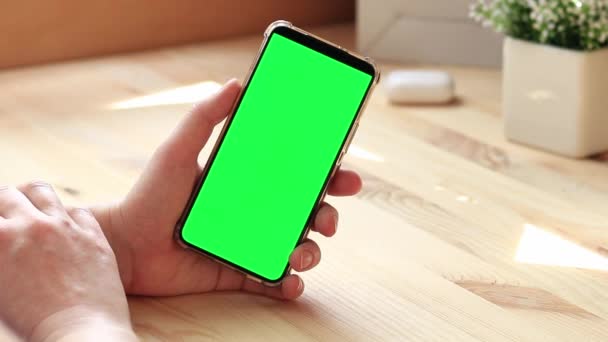 スマートフォンのクロマキーモックアップ アプリやウェブサイトのデザインのコピースペースを展示します 木のテーブルの背景に白い緑のスクリーンが付いているスマートフォンを握っている女性 スマートフォンの閉じる — ストック動画