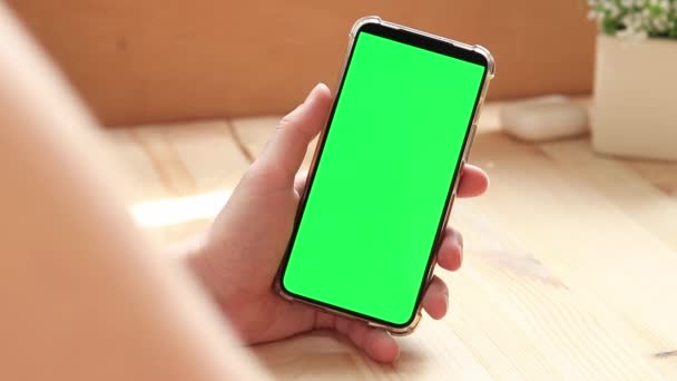 スマートフォンのクロマキーモックアップ アプリやウェブサイトのデザインのコピースペースを展示します 木のテーブルの背景に白い緑のスクリーンが付いているスマートフォンを握っている女性 スマートフォンの閉じる — ストック動画