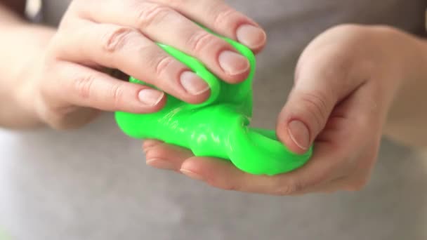这个女孩揉搓绿色黏液 女性的手的特写伸出明亮的绿色黏液 用于放松和冷静的抗压力玩具 一个有趣的感觉活动 玩具商店的概念 — 图库视频影像