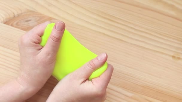 女孩把黄色的黏液跪在桌子的后面 女人的手伸出明亮的黄色黏液特写 一种用于放松的抗压玩具 一种逃避的方法 一种有趣的感觉活动 — 图库视频影像