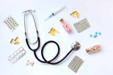 Beyaz arka planda steteskop, üst manzara. Tıbbi araç, farklı ilaçlar, haplar, kapsüller ve şırıngalar. Tıp ve sağlık hizmetleri kavramı. Auscultation aygıtı ve diyet takviyeleri
