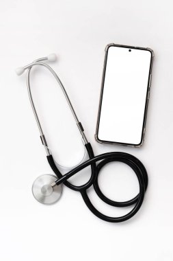 Beyaz arka planda steteskop ve beyaz beyaz ekranlı akıllı telefon. Tıbbi alet. Kardiyoloji ve tıp konsepti, sağlık hizmeti. Auscultation cihazı. Boş ekranlı telefon