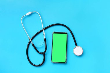 Mavi arka planda steteskop ve yeşil ekranlı akıllı telefon. Kardiyoloji ve sağlık konsepti. Auscultation cihazı. Kromatik cep telefonu modeli. Çevrimiçi tıbbi yardım kavramı