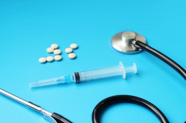Steteskop, haplar ve mavi arka planda şırınga, seçici odaklanma. Kardiyoloji ve sağlık konsepti. Auscultation cihazı. Tıbbi bakım konsepti. Tıbbi alet. Auscultation aparatı