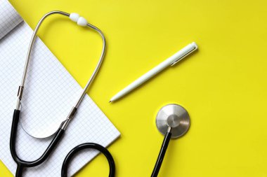 Stetoskop, not defteri ve kalem sarı arka planda, üst manzara. Kardiyoloji ve sağlık konsepti. Auscultation cihazı. Tıbbi bakım konsepti. Tıbbi alet. Auscultation aparatı