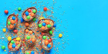 Şekerli çikolatalar ve mavi arka planda şeker renkli şekerler, üst manzara. Paskalya kompozisyonu. Masanın üzerinde yarım çikolatalı yumurta. Şenlikli tatlı ikram. Tatlılar