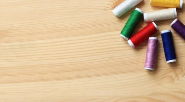Farklı renkte iplik makaraları, üst görünüm. Ahşap bir masanın üzerinde çeşitli renkli dikiş iplikleri, yakın plan. Dikiş