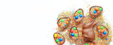 Çikolata yumurtaları ve tavşan, beyaz arka planda şeker renkli şekerler, üst manzara. Paskalya kompozisyonu. Paskalya çikolatalı tavşanı. Şenlikli tatlı ikram. Çikolata heykeli. Tatlılar