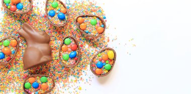 Çikolata yumurtaları ve tavşan, beyaz arka planda şeker renkli şekerler, üst manzara. Paskalya kompozisyonu. Paskalya çikolatalı tavşanı. Şenlikli tatlı ikram. Çikolata heykeli. Tatlılar