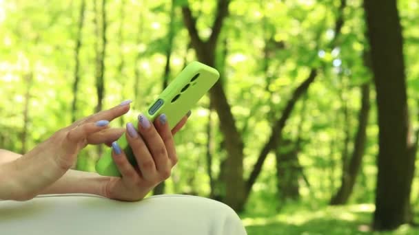 Mains avec un téléphone portable en gros plan. Surfez sur Internet. Une fille avec un téléphone dans le parc, l'été. Gros plan des mains féminines avec un smartphone. Concept de gadget de technologie moderne. Femme et téléphone