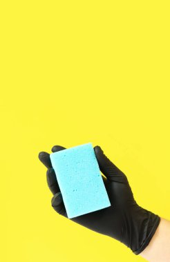 Sünger elinde, ıslak bir oda temizliği, parlak sarı arka plan. Mavi süngerli siyah lateks eldivenli bir adam eli. Temizlik. Bulaşıkları yıka. Temizlik servisi, temizlik.