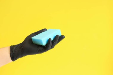 Sünger elinde, ıslak bir oda temizliği, parlak sarı arka plan. Mavi süngerli siyah lateks eldivenli bir adam eli. Temizlik. Bulaşıkları yıka. Temizlik servisi, temizlik.