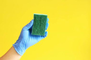 Bulaşık süngerli mavi lateks eldivenli bir adam eli. Mavi sünger elinde, odanın ıslak temizliği, sarı arka plan. Temizlik. Bulaşıkları yıka. Temizlik servisi, temizlik.