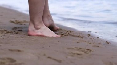 Sahilde çıplak kadın ayakları. Yazın nehrin yanında yürü. Suya yakın kumda duran insan ayaklarının yakın çekimi. Kumsal. Yazın nehirde dinlen. Bir kadın ayaklarını nehir suyunda ıslatıyor.