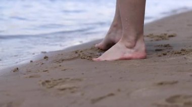 Sahilde çıplak kadın ayakları. Yazın nehrin yanında yürü. Suya yakın kumda duran insan ayaklarının yakın çekimi. Kumsal. Yazın nehirde dinlen. Bir kadın ayaklarını nehir suyunda ıslatıyor.