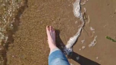 Çıplak kadın ayakları nehir sahilinde yürüyor, birinci şahıs manzaralı. Yazın nehrin yanında yürü. Kum ve suyun üzerinde yürüyen insan ayaklarının yakın çekimi. Yazın güzel havada yürü. Plaj